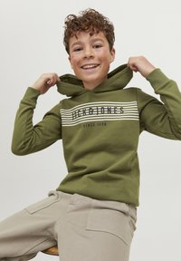 Sudadera verde con un logo y diseño a rayas en el pecho. Pantalones beige con bolsillos. El tejido parece suave con un ajuste casual.