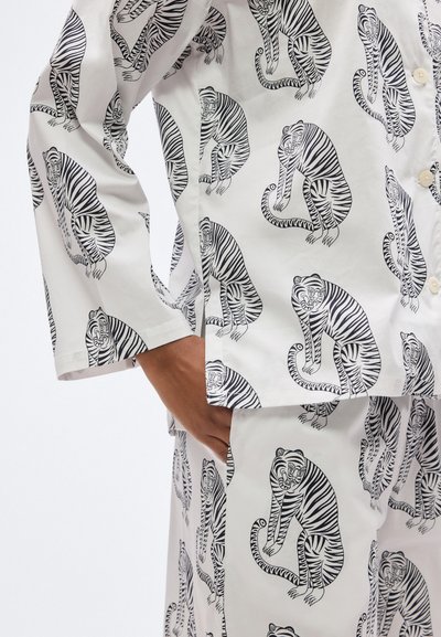 Σετ πιτζάμες από βαμβάκι ασπρόμαυρο με επαναλαμβανόμενο μοτίβο τίγρης· περιλαμβάνει πουκάμισο με κουμπιά και μανίκια τριών τετάρτων και παντελόνια που ταιριάζουν.