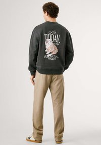 Sudadera gris con un gráfico de bulldog y texto en la parte posterior. Combinada con pantalones beiges y calzado casual.