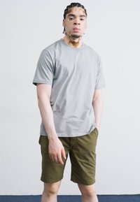 T-shirt gris à manches courtes en tissu lisse, associé à un short vert olive. Design simple avec une coupe décontractée et des couleurs neutres.