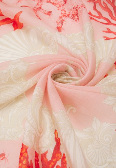 Šilkinis šalikas švelnios rožinės spalvos pagrindu, su sudėtingais baltais gėlėmis ir ryškiomis koralinėmis akcentais, švelniai suvyniotas spirale.