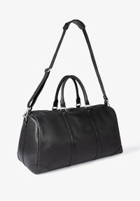 Schwarze Lederreisetasche mit zwei oberen Griffen, einem abnehmbaren Schulterriemen und silberner Beschläge. Glatte Textur und abgerundete Form.