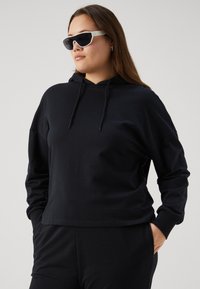 Felpa nera in cotone con vestibilità rilassata, cappuccio con coulisse e maniche lunghe. Abbinata a occhiali da sole bianchi eleganti per un look contrastante.