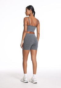 Szary sportowy crop top i wysokie szorty wykonane z teksturowanej tkaniny. Modelka ma na sobie białe sneakersy i skarpetki do kostek, widok z tyłu.
