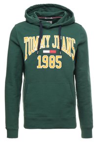 Green hoodie featuring a front pocket, drawstring hood, and bold yellow text "TOMMY JEANS 1985" with a small red and white logo detail.