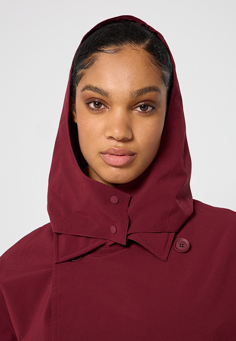 Bordeauxkleurige hooded jas met een hoge kraag, voorzien van grote knopen en een gladde textuur. Ontworpen voor warmte en weersbestendigheid.