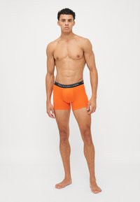 Oranžni bombažni bokserji z gačkami črne barve, na katerih je napis "POLO RALPH LAUREN." Oblikovanje vključuje prilegnjeno silhueto s kratkimi nogavicami.