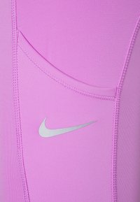 Tela deportiva rosa con detalle de bolsillo lateral y costura plana. Presenta un logo plateado de Nike en la sección inferior izquierda.