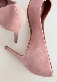 Tacones altos de ante rosa con punta afilada y tacón de estilete. Textura suave y un ligero brillo. Presenta un corte en el lado.