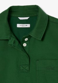 Grünes Baumwollpolohemd mit klassischem Kragen, drei weißen Knöpfen und einer Brusttasche links mit gesticktem Logo. Reguläre Passform.