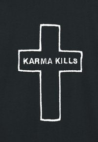 Tela negra con una cruz blanca bordada y el texto "KARMA KILLS" centrado en el brazo horizontal. Textura suave con colores contrastantes.