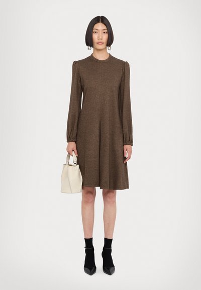 Räppäristä long-sleeve mekko ruskeasta, tekstiili on teksturoitu ja A-linjan siluetti on väljä. Parinaan pieni valkoinen käsilaukku ja mustat korkokenkäsukat.
