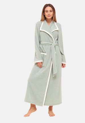 Woman standing barefoot wearing a light green full-length robe with white trim, belted waist, and large front pocket on a plain background.