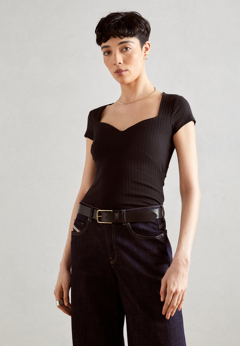 Haut noir à manches courtes côtelé avec un col carré, associé à un pantalon en denim foncé et une ceinture noire avec une boucle dorée.