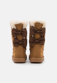 Bottes en daim marron avec doublure en fourrure blanche, ornées de trois grands nœuds en satin marron à l'arrière, semelles en caoutchouc légères et détail de logo.