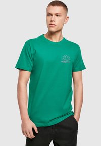 Grøn bomulds t-shirt med korte ærmer, rund halsudskæring og en lotusgrafik. Har en afslappet pasform og en glat tekstur.