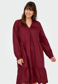 Burgundy cotton dress with long sleeves, a V-neck, and embroidered accents along the yoke and hem, featuring a flared, gathered skirt.