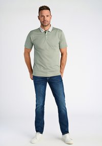 Ljusgrön pikétröja med kontrasterande krage och tre knappar, som är i kombination med blå jeans och vita sneakers. Slät textur, avslappnad passform.