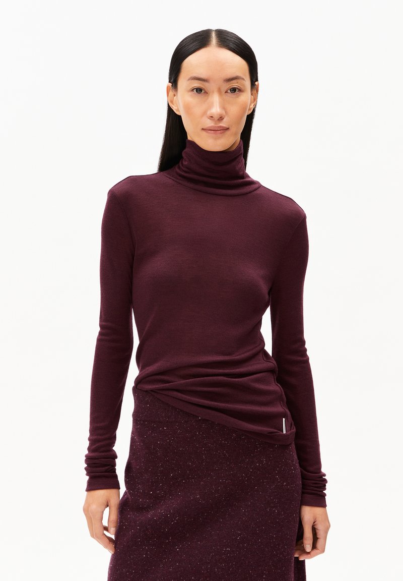 Top moulant bordeaux à col roulé avec des manches longues, fabriqué à partir d'un tissu lisse et léger. Assorti à une jupe tricotée texturée du même ton.