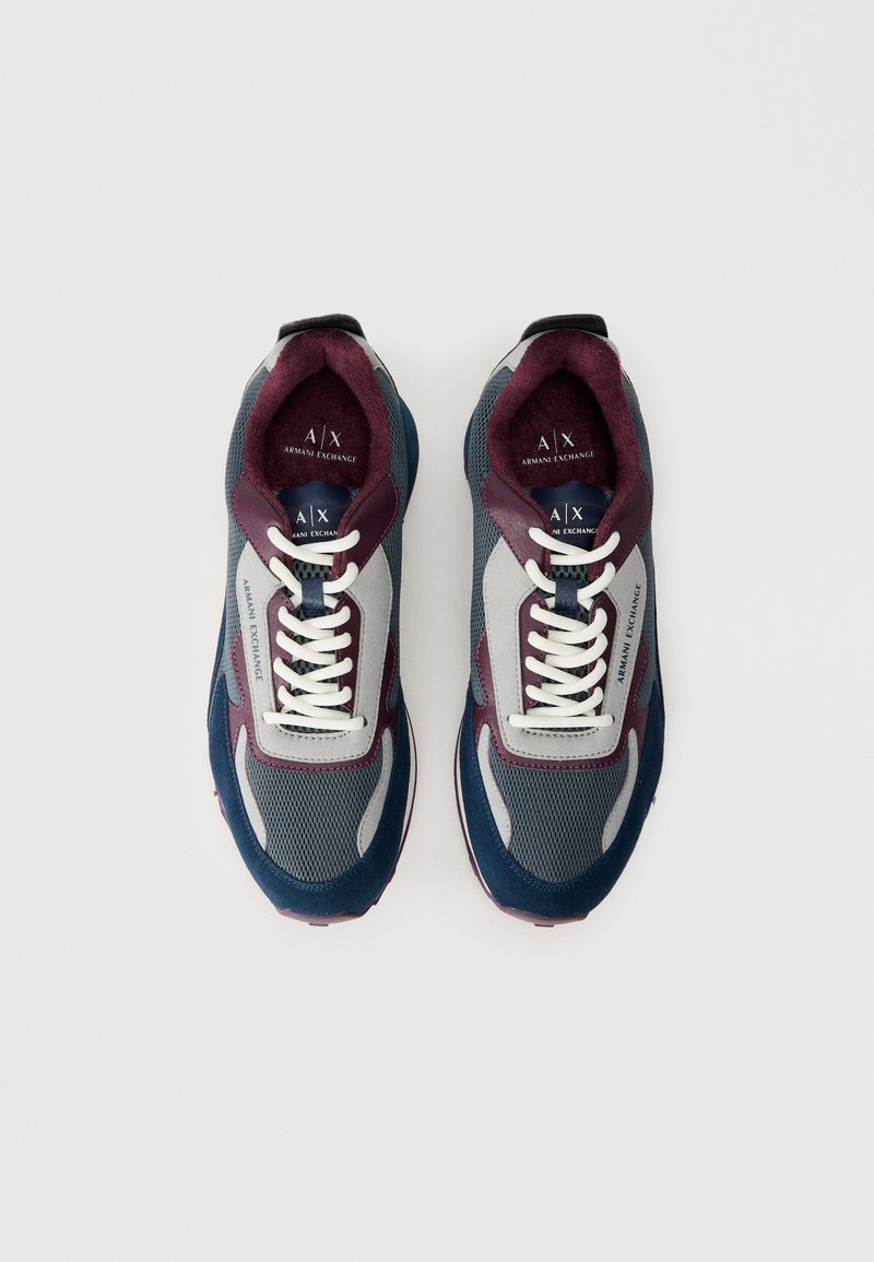 Une paire de baskets Armani Exchange grises, marines et bordeaux avec des lacets blancs, des détails en mesh et en daim, vue de dessus sur un fond blanc.