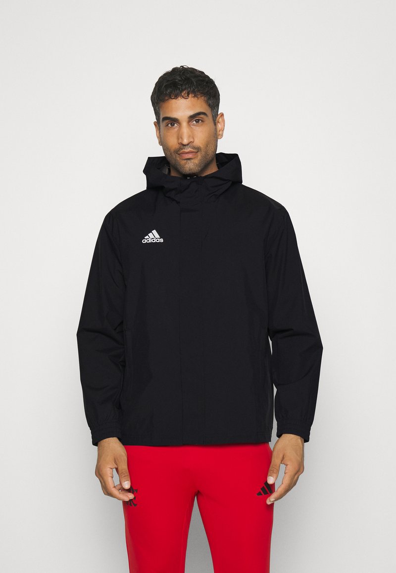 Czarna, kapturowa kurtka przeciwdeszczowa z pełnym zamkiem, elastycznymi mankietami oraz białym logo Adidas na górnej lewej stronie. Gładka tekstura i lekka konstrukcja.