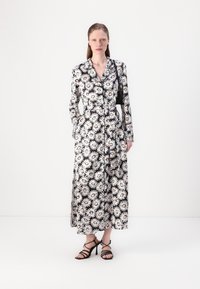 Maxime dressi mustalla ja valkoisella päivänkakkarakuviolla, kauluksella, pitkät hihat, nappikiinnitys ja kaksi sivutaskua. Yhdistetty mustiin hihnakenkiin.