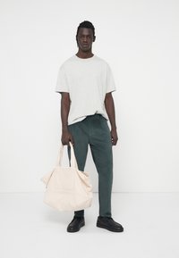 Lichtgrijze katoenen T-shirt, donkergroene corduroy broek, zwarte schoenen en een lichtroze tote bag met een voorzak en handvatten.