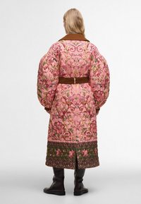 Pletený dlouhý kabát v růžové barvě s květinovou výšivkou, hnědým páskem a límcem. Má nafouknuté rukávy a vzorovaný lem s zelenými akcenty.