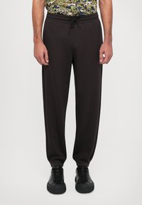 Black sweatpants with an elastic waistband and drawstring tie, featuring tapered legs and side pockets, made from soft fabric.