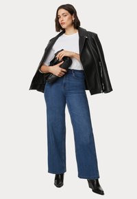 Svart läderbikerjacka, vit t-shirt och blå vida jeans. Modellen håller i en svart clutch. Svarta stövletter med klack fulländar looken.