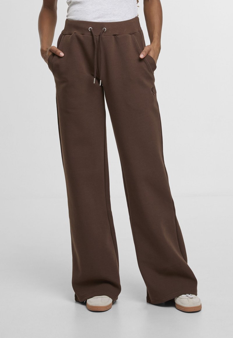 Pantalones deportivos marrones de tela suave, con cintura de cordón, bolsillos laterales y un ajuste relajado con pierna ancha.