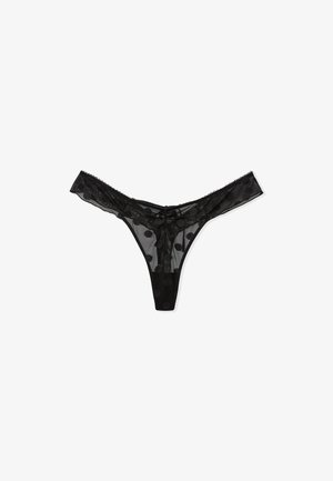 Black thong made of sheer mesh fabric with polka dot pattern. Features scalloped edges and a minimalistic design.