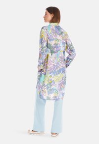 Langarmhemd mit einem mehrfarbigen, tropischen Muster in Lila-, Grün- und Blautönen. Verfügt über einen Kragen und seitliche Schlitze.