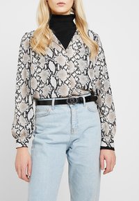Langærmet bluse med et slangemønster i beige og sort, parret med lyseblå højtaljede jeans og et sorte bælte med en dobbelt ring.