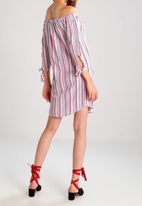 Off-shoulder stripe dress in white, red, and blue; features tied sleeves. Red strappy heels have a block heel and ankle ties.