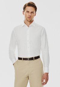 Biała, długorękawowa koszula zapinana na guziki z kołnierzykiem, gładka w dotyku, w połączeniu z beżowymi spodniami i brązowym paskiem. Prosty design, bez wzorów.