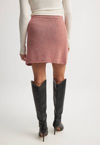 Pletena krilo v roza-oranžni barvi s prilegajočim pasom in razširjenim robom. Ujemajo se z črnimi usnjenimi škornji do kolen z koničastimi vrhovi.