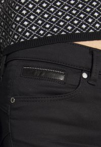 Svarta jeans i denim med en texturerad svart läderlapp, silverdetaljer och stickningsdetaljer. Tröjan ovan har ett geometriskt svartvitt mönster.