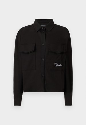 Chemise noire à manches longues en coton, avec un col boutonné, deux poches poitrine et un logo brodé sur le côté gauche.