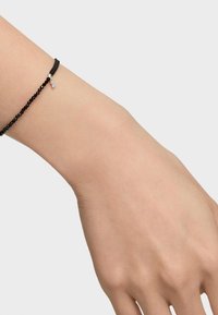 Pulsera de cuentas negras en una muñeca, con un pequeño charm de plata. Las cuentas son redondas y suaves, ofreciendo una apariencia texturizada.