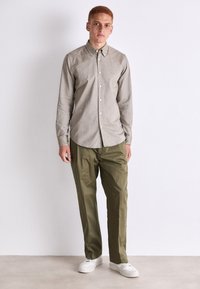Camisa de botones gris claro con mangas largas, combinada con pantalones verde oliva y zapatillas blancas. Tejido suave y corte informal.
