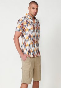 Chemise multicolore à manches courtes avec un motif abstrait audacieux. Short cargo beige avec poches latérales. Tissu lisse et décontracté.