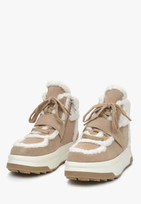 Beige suède hoge sneakers met witte schapenvacht accenten, textuurveters en een stevige witte zool, voorzien van een zijrits.