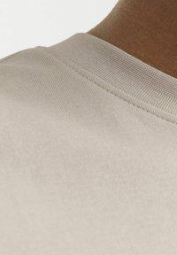 Camiseta de algodón beige claro con un escote redondo y un acabado texturizado, además de costuras visibles a lo largo del collar.