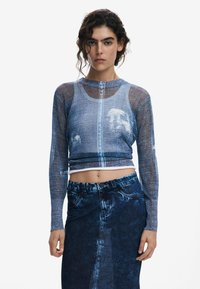 Blue mesh long-sleeve top with denim pattern; cropped design. Paired with high-waisted denim skirt. Textured fabric with visible seams.
