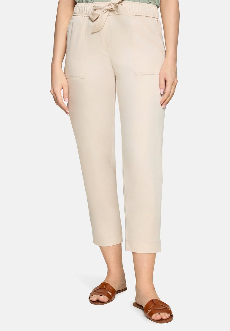 Pantalon beige court taille haute avec poches avant et taille à cordon, porté avec des sandales marron en cuir à enfiler.