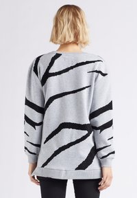 Felpa grigia con un motivo a strisce zebra nere testurizzate. Maniche lunghe, polsini a costine e una vestibilità rilassata con orlo arrotondato.