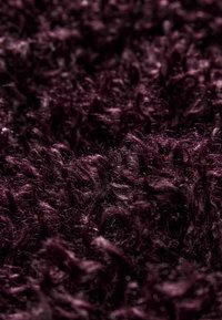 Dettaglio ravvicinato di un tessuto morbido, riccio e di un viola scuro, con un aspetto peloso e soffice.