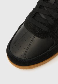 Μαύρο αθλητικό παπούτσι με λείο δέρμα στη μύτη και επικάλυψη από σουέντ με υφή. Διαθέ τει μαύρα κορδόνια και σόλα από καουτσούκ χρώματος καραμέλας.