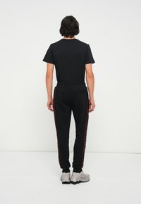Camiseta negra de manga corta combinada con pantalones jogging negros que tienen franjas laterales rojas. El material es suave, con una cinturilla elástica y bolsillos.
